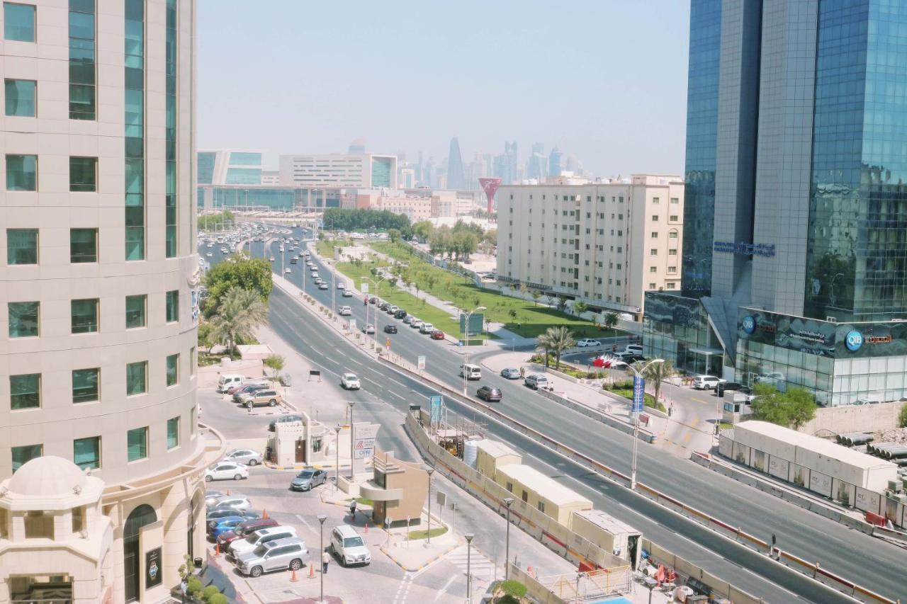 Hotel Millennium Plaza Doha Exterior foto The photo shows a cityscape featuring a wide road with moving vehicles, flanked by modern buildings. There are multiple lanes on the road, with greenery and landscaped areas visible in the median. In the distance, a skyline with tall buildings is par