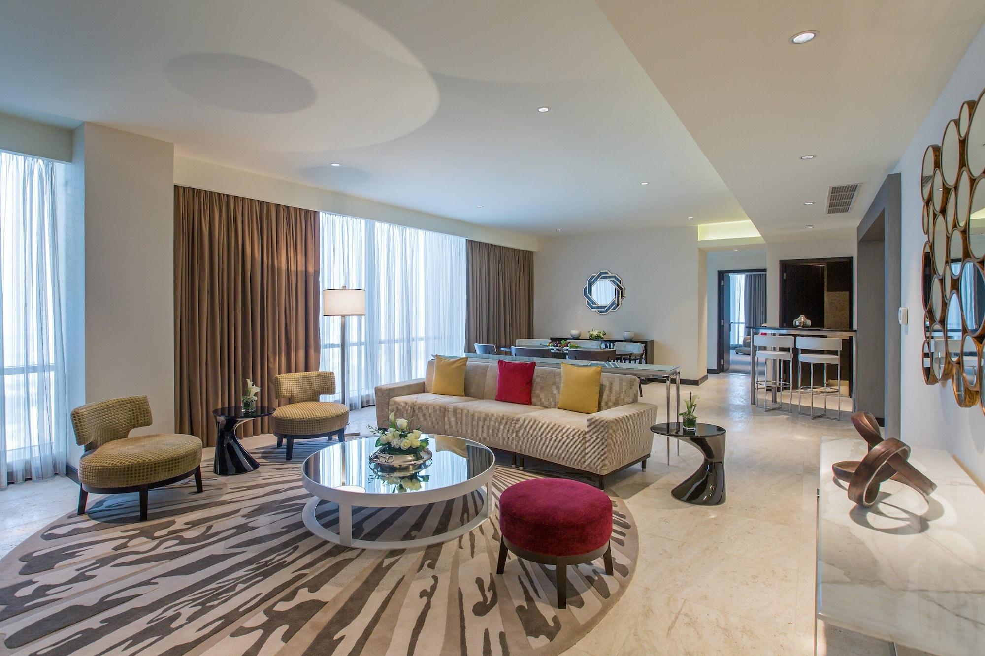 Hotel Millennium Plaza Doha Exterior foto The photo shows a stylish and modern living room interior. It features a light-colored sofa with colorful throw pillows, a round coffee table in the center, and several lounge chairs arranged around it. The seating area is situated on a patterned rug