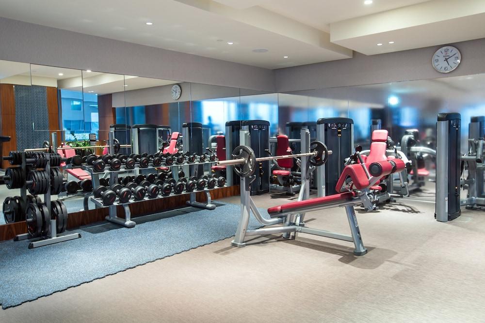 Hotel Millennium Plaza Doha Exterior foto The photo shows a gym interior. It features a variety of fitness equipment, including weight benches and a rack of dumbbells. The gym has a modern design with a clean layout. There are mirrors on the walls, enhancing the space and allowing users to m