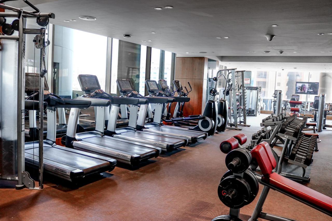 Hotel Millennium Plaza Doha Exterior foto The photo shows a gym interior with various exercise equipment. On one side, there are several treadmills lined up, with large windows allowing natural light to enter the space. In the background, you can see additional fitness machines and weights, 