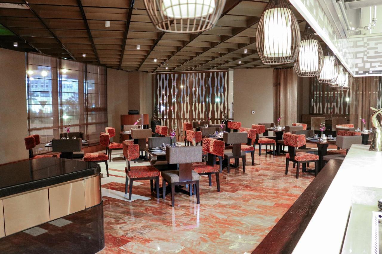 Hotel Millennium Plaza Doha Exterior foto The photo shows an elegantly designed restaurant interior. It features wooden tables and chairs arranged throughout the space, with a warm color palette of browns and reds. The flooring is made of polished tiles that add to the upscale atmosphere. Th