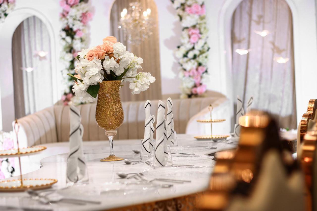 Hotel Millennium Plaza Doha Exterior foto The photo depicts a beautifully arranged dining table set for an elegant occasion. The centerpiece features a large, ornate vase filled with a variety of flowers, including soft pink and white blooms. The table is adorned with neatly folded napkins a