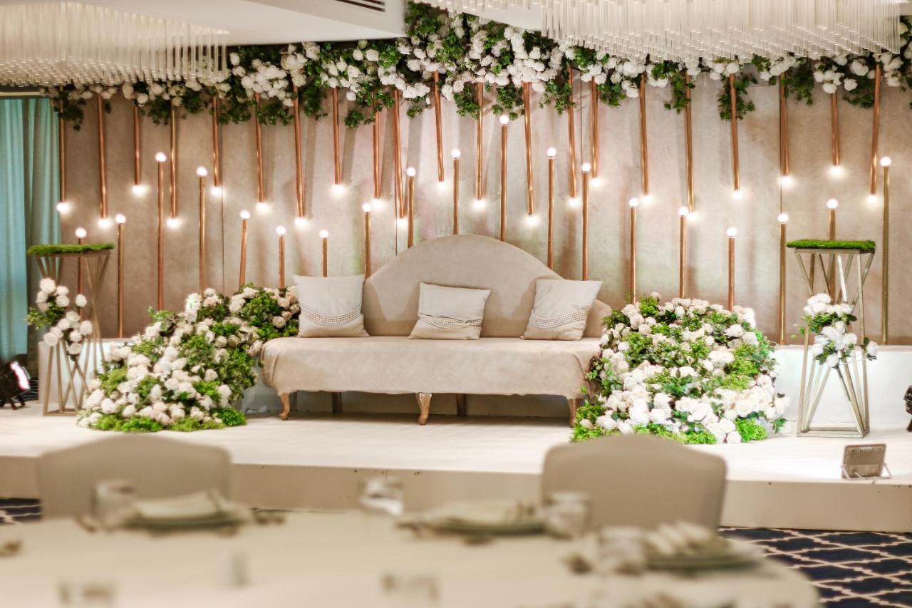 Hotel Millennium Plaza Doha Exterior foto The photo depicts a beautifully decorated setting, likely for a wedding or a special event. In the center, there is a stylish sofa with several cushions arranged on it. Surrounding the sofa are lush floral arrangements with white flowers and greenery