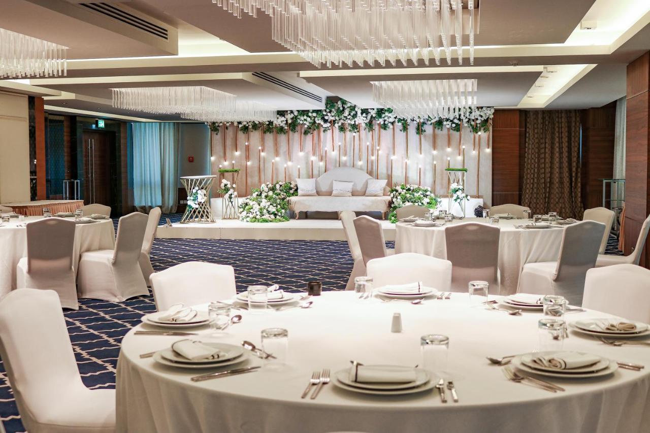 Hotel Millennium Plaza Doha Exterior foto The photo shows an elegantly set banquet hall or event space. In the foreground, there are round tables dressed in white tablecloths, each with neatly arranged place settings, including plates and glasses. The background features a beautifully decora