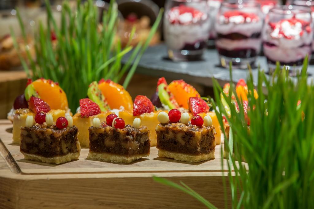 Hotel Millennium Plaza Doha Exterior foto The photo shows a beautiful display of desserts. In the foreground, there are several small pastry squares topped with fruits and decorative elements, showcasing a variety of colors. There are also slices of orange and kiwi placed beside the pastries