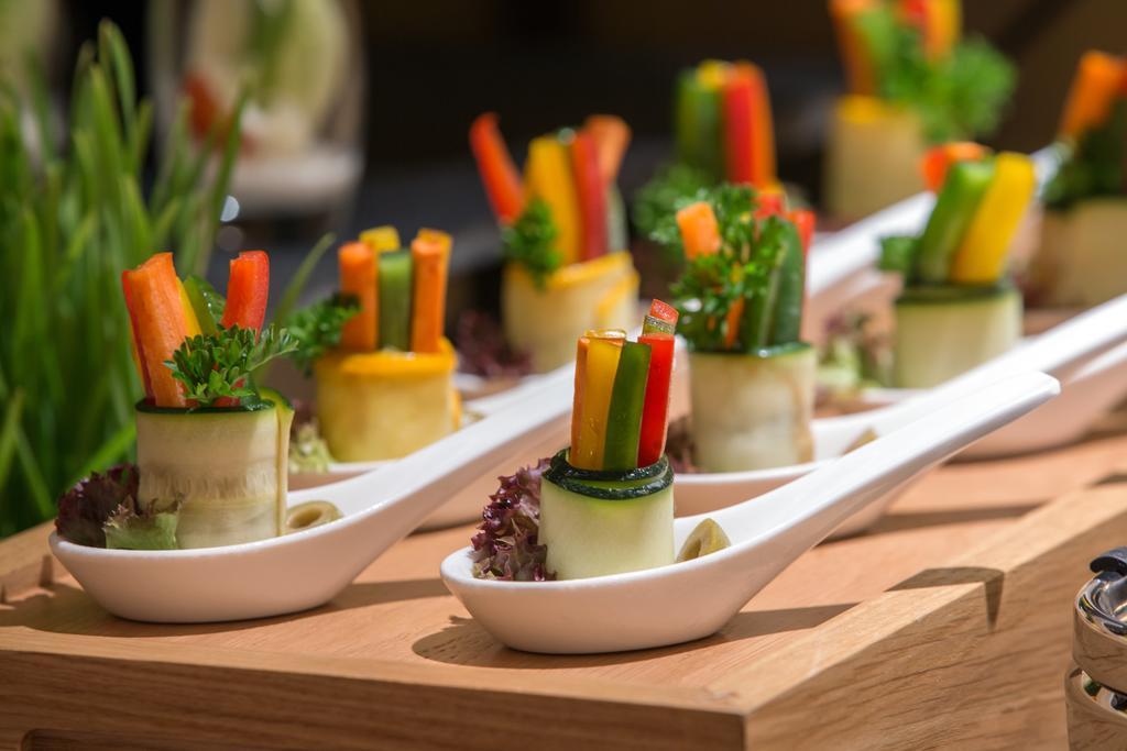 Hotel Millennium Plaza Doha Exterior foto The photo showcases a presentation of gourmet hors d'oeuvres. Each piece consists of a rolled cucumber or zucchini filled with various colorful vegetables like carrots, bell peppers, and possibly herbs, arranged neatly on a white tasting spoon. The d