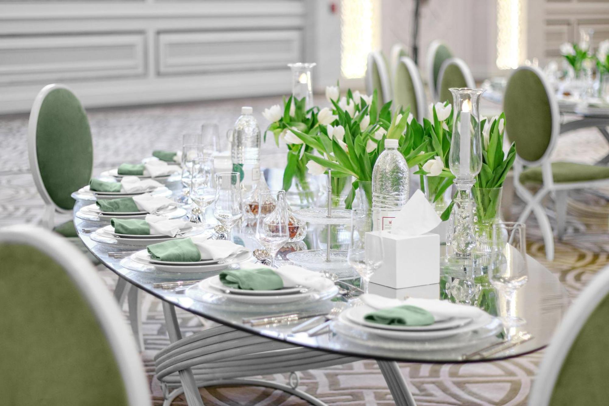 Hotel Millennium Plaza Doha Exterior foto The photo shows an elegantly set dining table. The table is oval, with a glass top and arranged with multiple place settings. Each setting includes a plate, a folded napkin, and drinking glasses. There are small vases filled with green tulips as deco