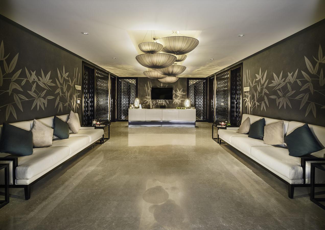 Hotel Millennium Plaza Doha Exterior foto The photo depicts a modern and elegant lobby or waiting area. The walls are adorned with stylish, dark-colored wallpaper featuring a bamboo motif. In the center of the space, there are several large, artistic light fixtures hanging from the ceiling, 