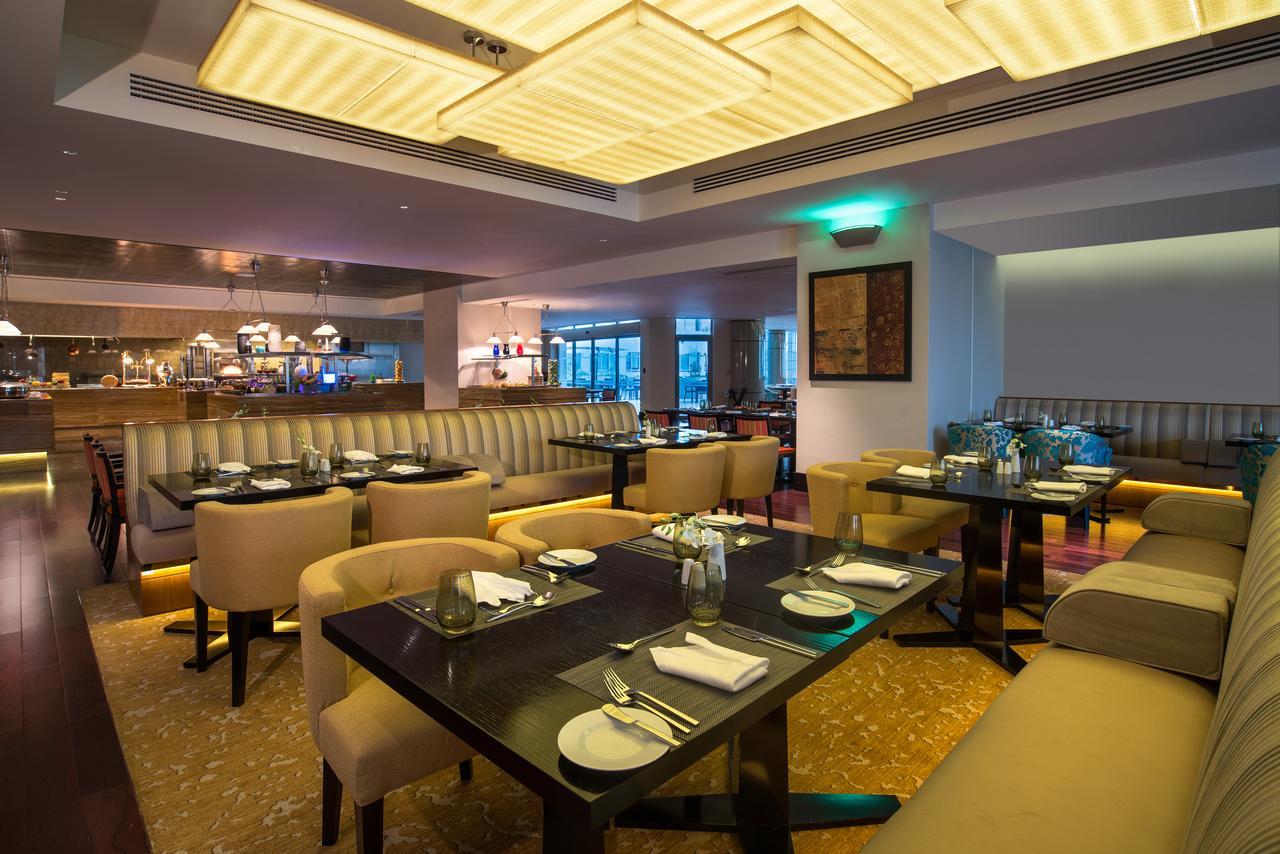 Hotel Millennium Plaza Doha Exterior foto The photo shows a modern restaurant interior. The space features elegant seating arrangements with beige upholstered chairs and tables surrounded by a warm, inviting atmosphere. The decor includes a combination of soft lighting, highlighted by a dist