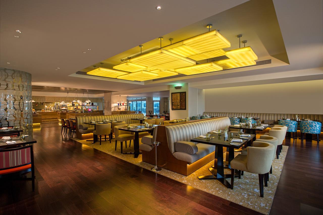 Hotel Millennium Plaza Doha Exterior foto The photo shows the interior of a modern restaurant. It features a spacious dining area with elegant seating arrangements, including plush booths and tables with chairs. The decor includes warm wooden flooring and stylish lighting, notably a large, i