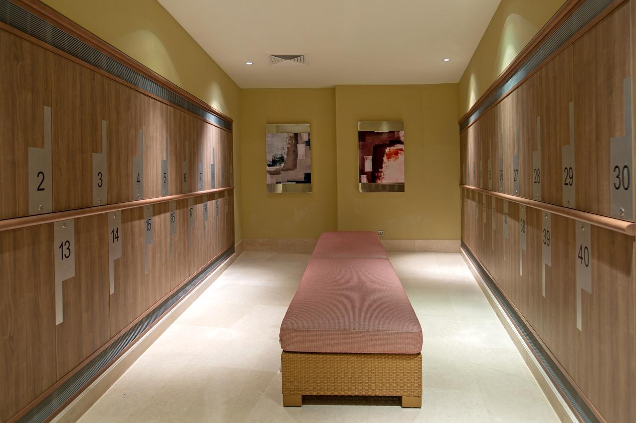 Hotel Millennium Plaza Doha Exterior foto The photo shows a modern locker room or changing area. On either side, there are wooden lockers numbered from 1 to 24, providing storage for personal items. In the center, there's a long, cushioned bench for seating. The walls are painted in a light 