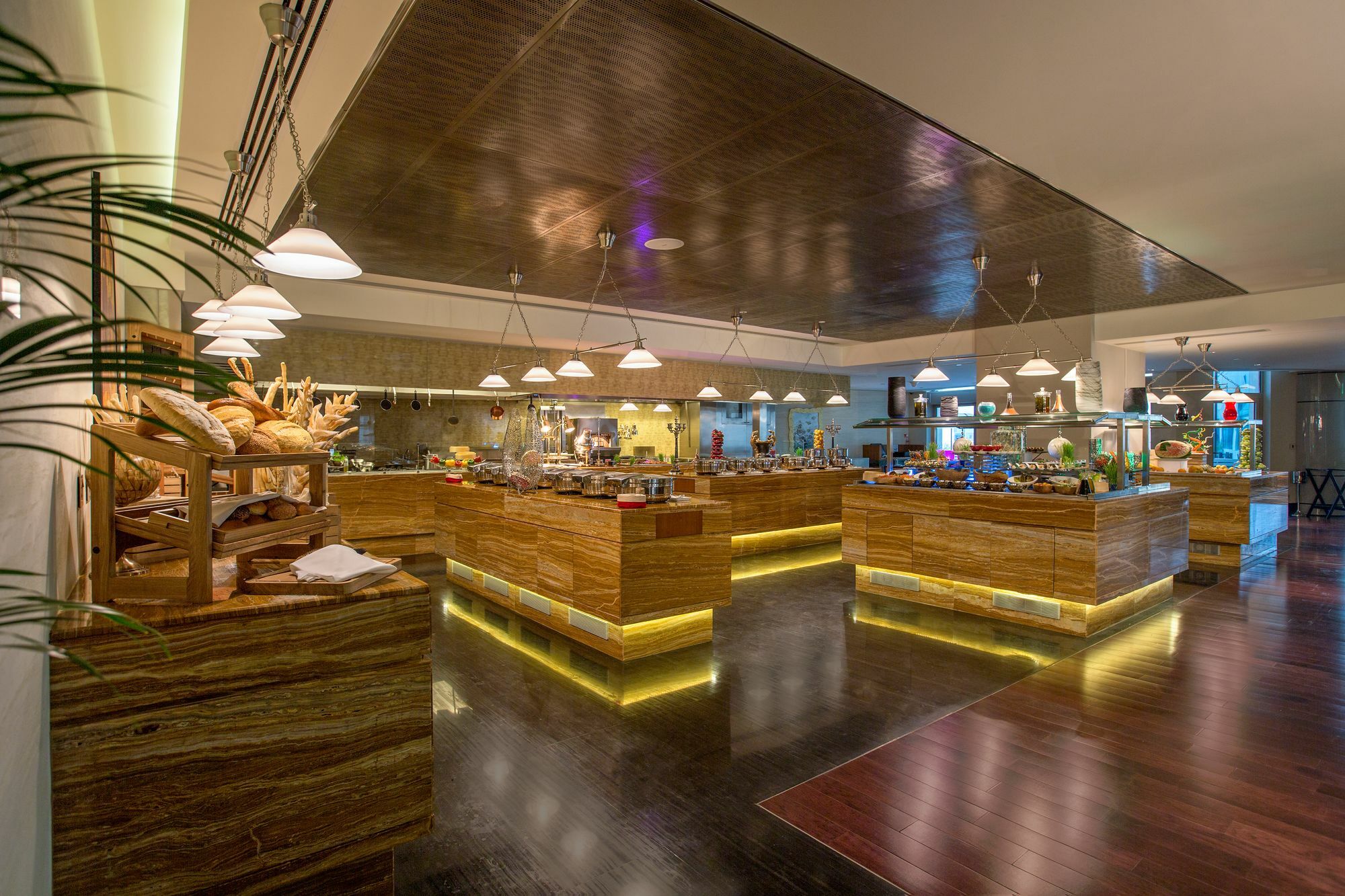 Hotel Millennium Plaza Doha Exterior foto The photo depicts a spacious and elegantly designed dining area, likely in a restaurant or buffet setting. The interior features warm wooden furnishings and modern lighting. Several wooden serving stations are illuminated with soft lights, showcasing